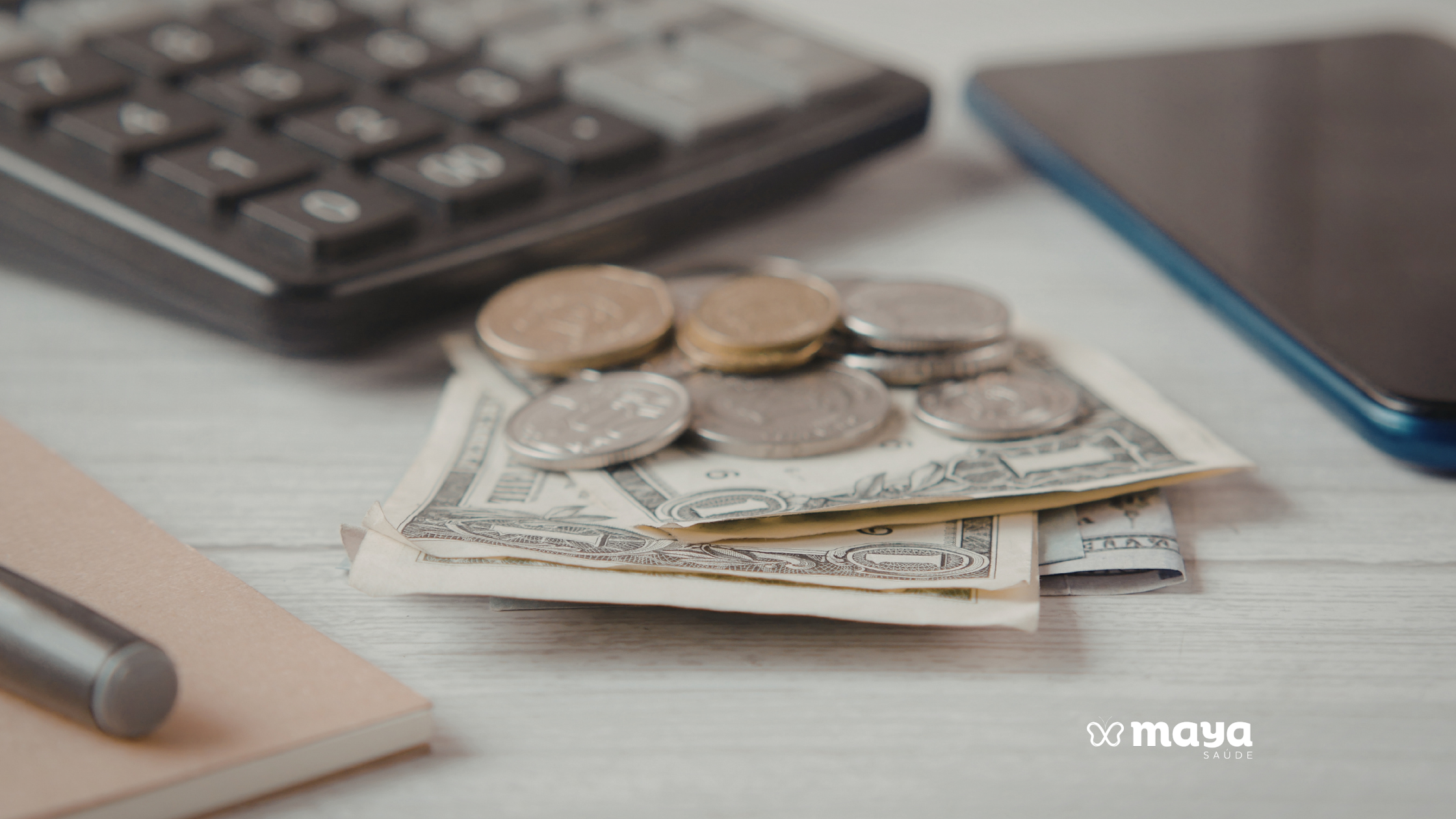 Moedas e notas de dinheiro sobre a mesa ao lado de uma calculadora, um celular e um caderno, ilustrando quanto custa um cuidador de idosos.